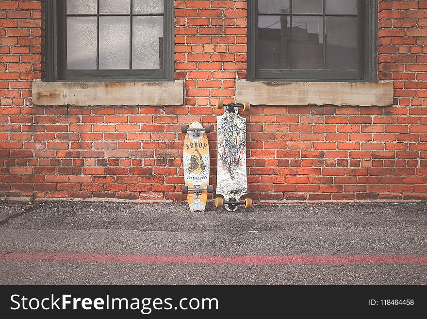 Two White and Brown Longboard Leaning on Brown Bricks Wall