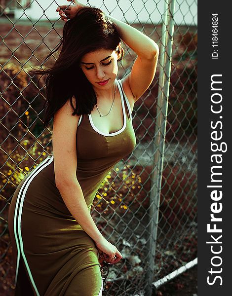 Woman in Green Sleeveless Dress Leaning on Grey Link Fence