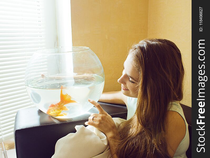 Pretty woman playing with goldfish at home, sunlight morning