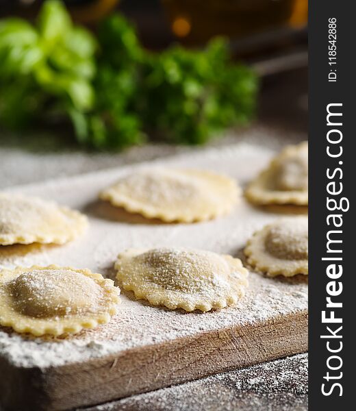 Uncooked tortelli with cheese filling on a wooden board.
