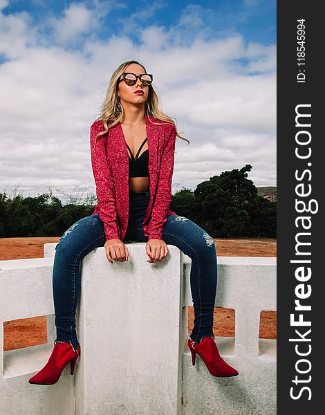 Woman Wearing Red Jacket and Distressed Blue Denim Skinny Jeans Sitting on Bench