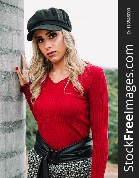 Woman Wearing Black Cap and Red V-neck Sweatshirt Near Concrete Wall