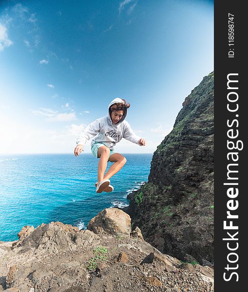 Man Wearing Gray Hoodie Jumping At Rock