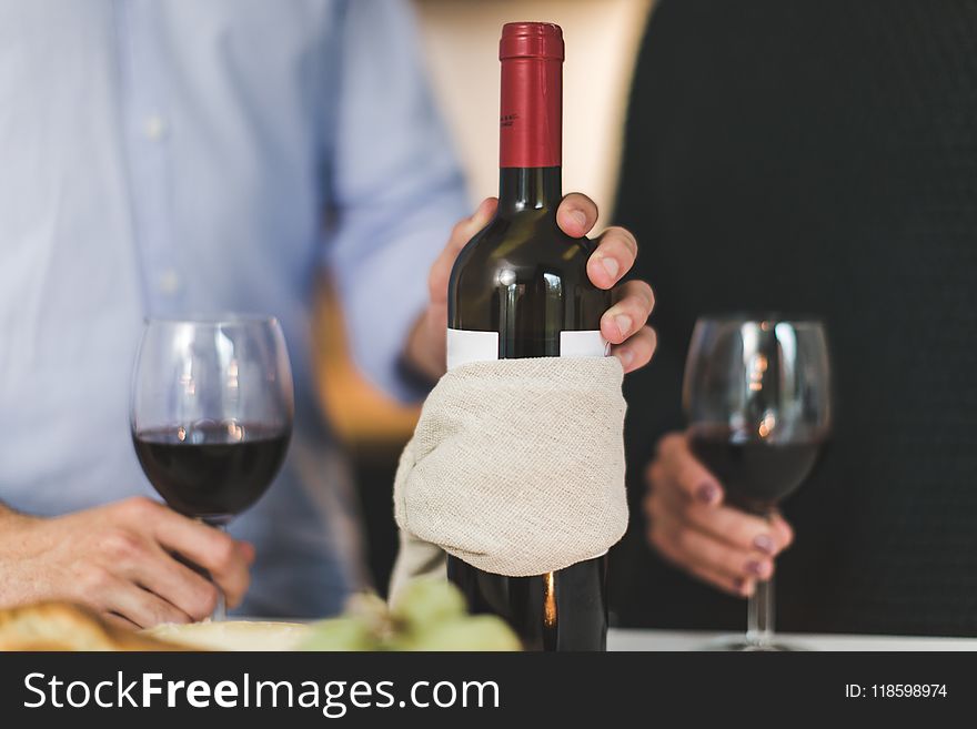 Man Holding White Labeled Red Wine Bottle Near Wine Glasses