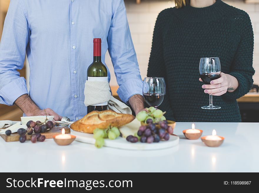 Man Standing Beside Woman Holding Wine Glass in Front of Grapes and Bread on Table