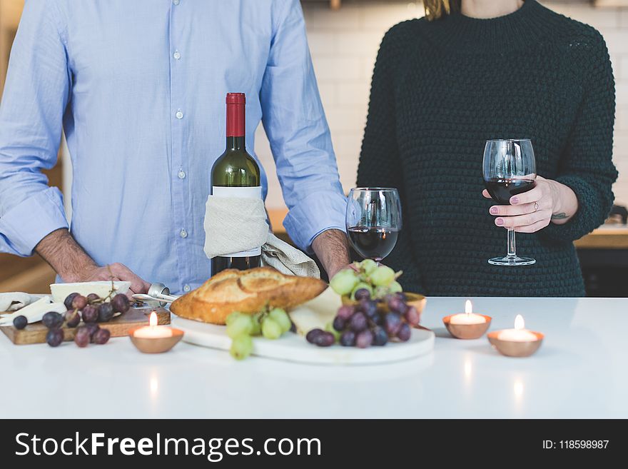 Man Standing Beside Woman Holding Wine Glass In Front Of Grapes And Bread On Table