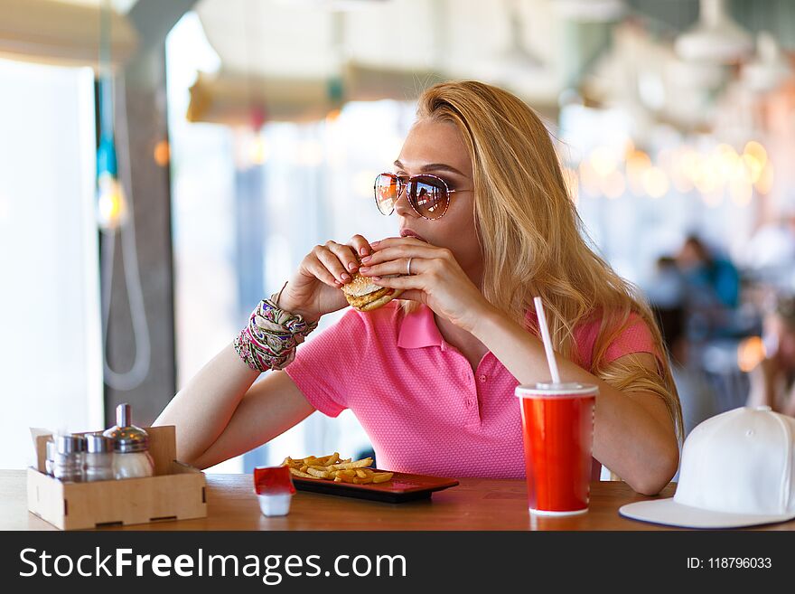 Young pretty woman resting in cafe and eating burger