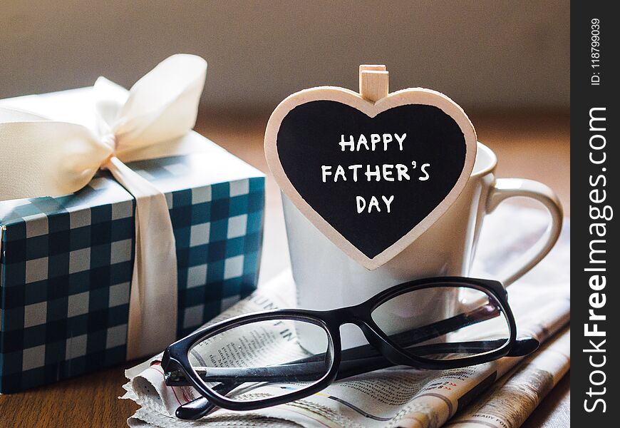 Happy fathers day concept. coffee cup with gift box, heart tag with Happy father`s day text and newspaper, glasses on wooden table background.