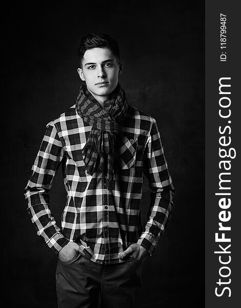 Portrait of young trendy handsome man with short dark hair wearing checkered shirt and brown trousers standing and posing against gray concrete wall. Portrait of young trendy handsome man with short dark hair wearing checkered shirt and brown trousers standing and posing against gray concrete wall