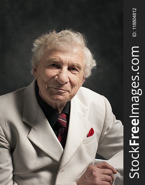 Portrait of a senior charismatic man in a white suit with a black shirt and red tie on a gray background. Portrait of a senior charismatic man in a white suit with a black shirt and red tie on a gray background