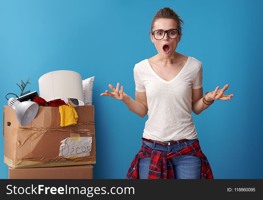 Shocked woman with an untidy cardboard box in background on blue