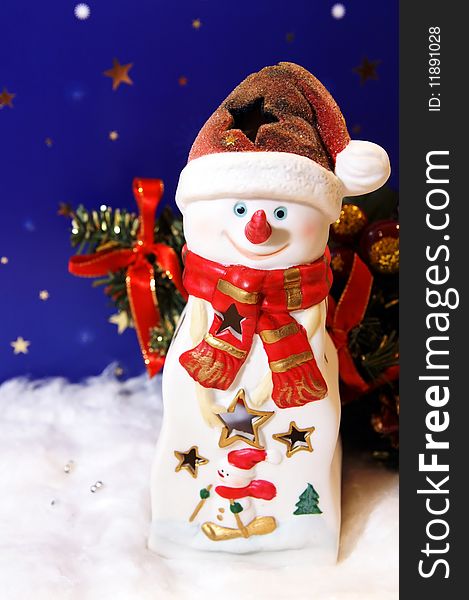 Funny snowman against a festive night background for a New Year card on a white snow, arranged with colorful New Year's tree. Funny snowman against a festive night background for a New Year card on a white snow, arranged with colorful New Year's tree