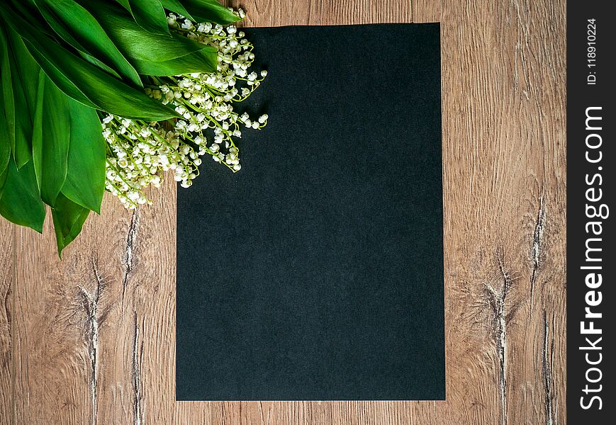 Bouquet of lilies of the valley on a wooden background and an empty piece of black paper.