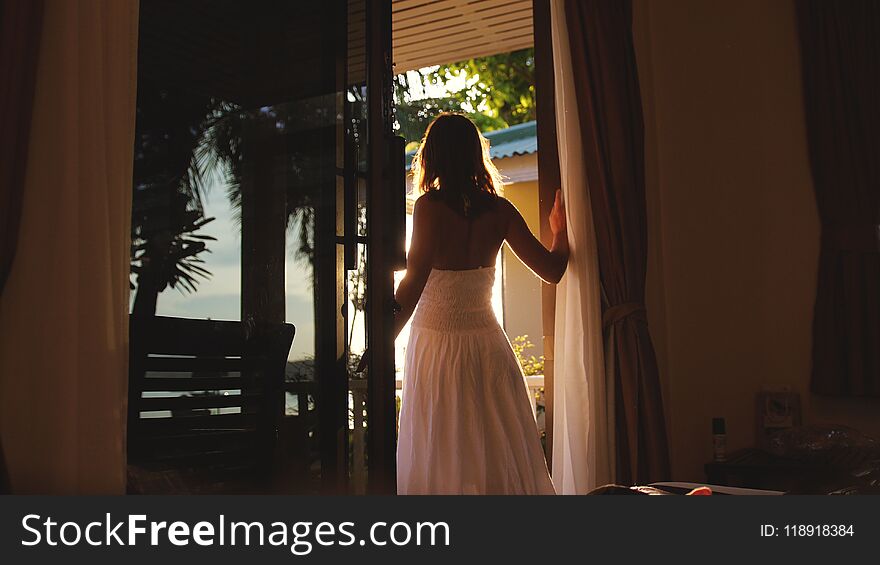 Brunette girl stands in the doorway in the early morning during sunrise with lens flare effects