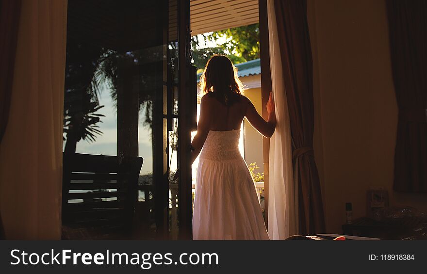 Brunette Girl Stands In The Doorway In The Early Morning During Sunrise With Lens Flare Effects