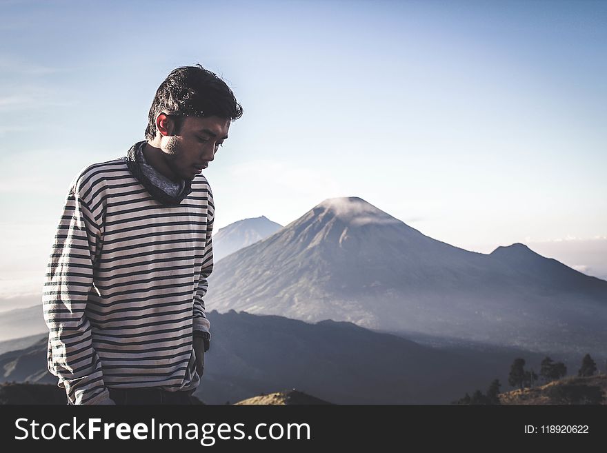 Person Wearing White and Black Striped Sweatshirt Standing in Front of Mountains