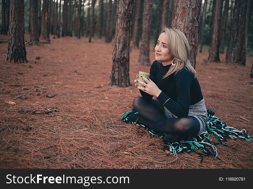 Woman in Black Sweater Sitting on Brown Ground While Holding Cup