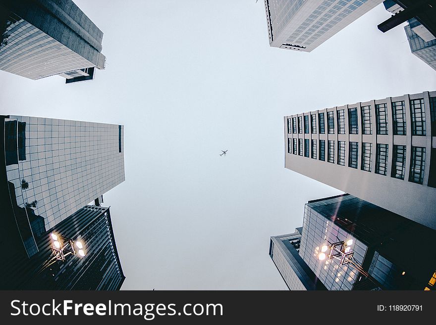 Low Angle Photography of Airplane Flying Above High Rise Buildings