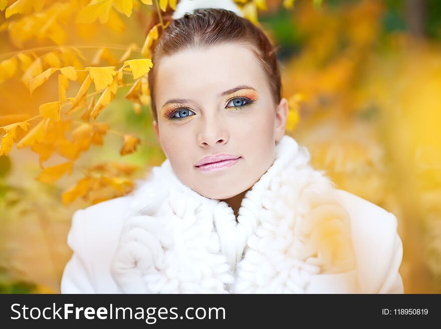 Young lady wearing white sweater among golden leaves