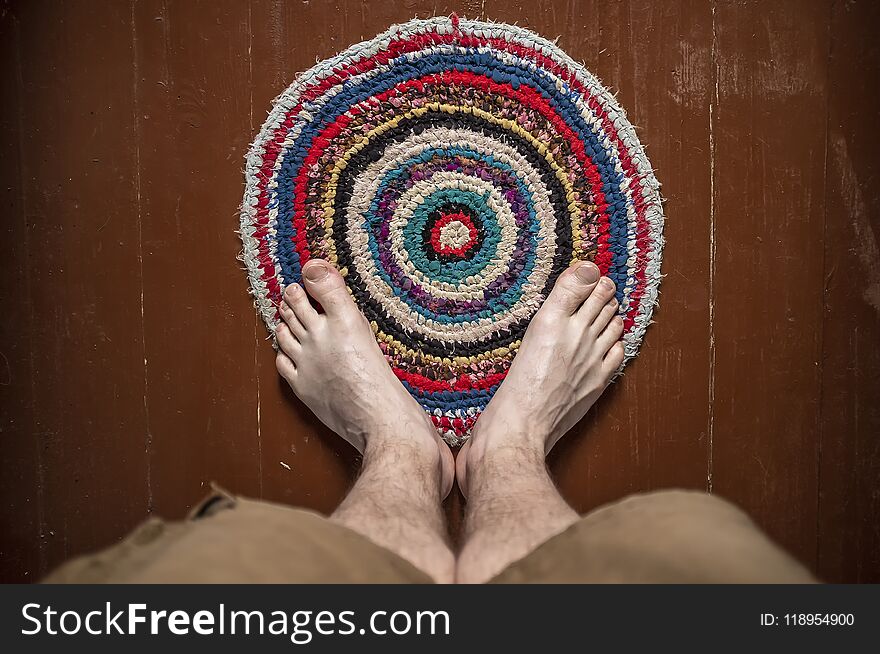 Legs men stand on a beautiful round homemade knitted colored rug. Close-up.