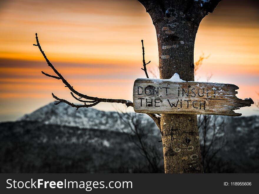 Old warning sign on the tree against witches in front of mountain at sunset, Bergen, Norway. Old warning sign on the tree against witches in front of mountain at sunset, Bergen, Norway