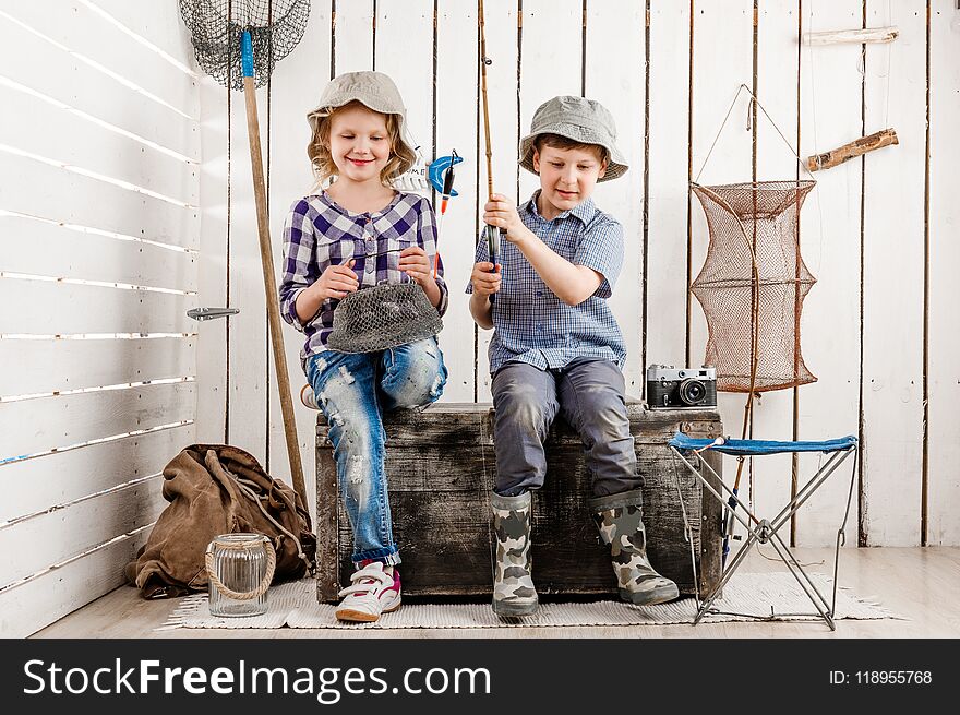 Two little children sitting on big old chest with net and rod in hands