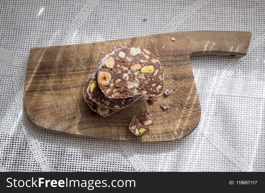 Slices of chocolate cake with hazelnuts and pistachios. Resting on a rustic wooden cutting board. View from above. Slices of chocolate cake with hazelnuts and pistachios. Resting on a rustic wooden cutting board. View from above.