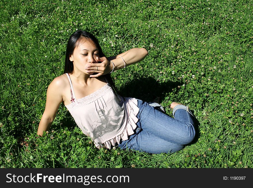 Young asian woman sitting on grass is kissing. Young asian woman sitting on grass is kissing