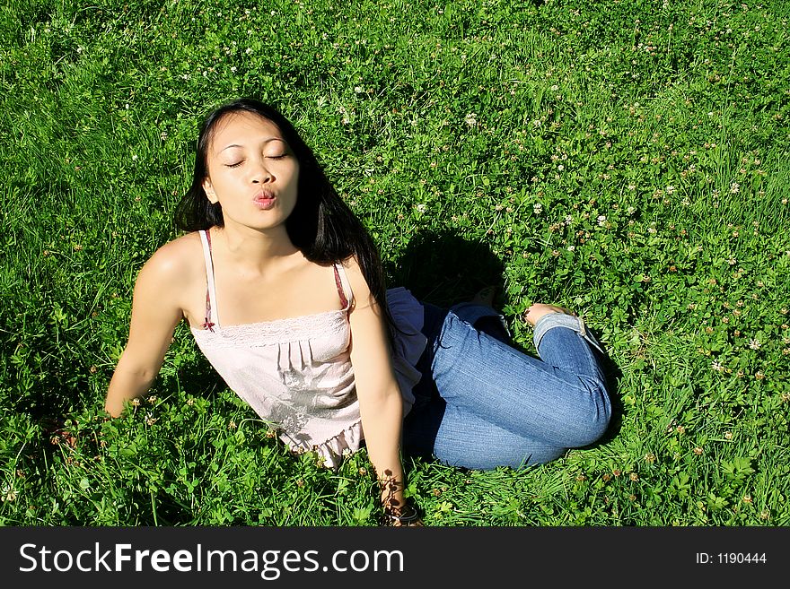 Asian young woman with long black hair sitting on grass is kissing. Asian young woman with long black hair sitting on grass is kissing