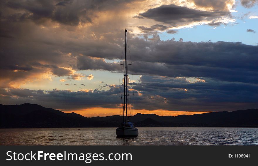 Orange blue sunset over the sea with black mountains, rain clouds and sailboat centered. Orange blue sunset over the sea with black mountains, rain clouds and sailboat centered