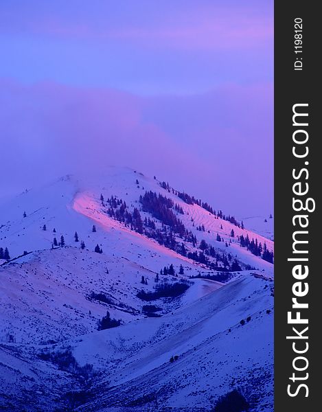 Snow covered mountains peaks with soft pink sunset, sunrise sunlight light on it with clouds. Snow covered mountains peaks with soft pink sunset, sunrise sunlight light on it with clouds