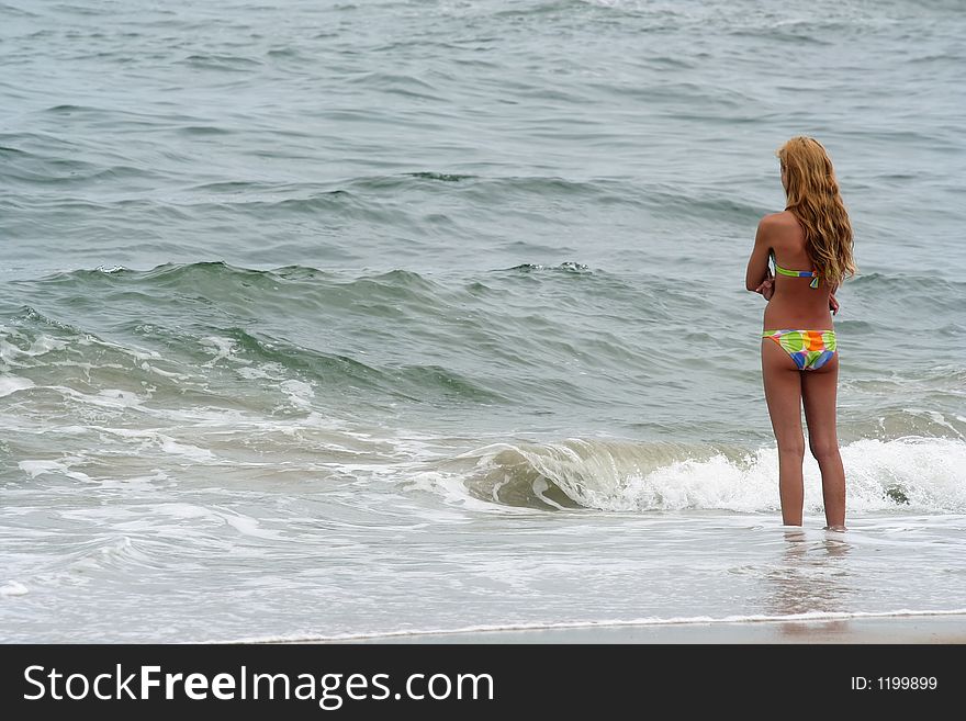 Young girl standing at the ocean's edge with surf at her feet. Young girl standing at the ocean's edge with surf at her feet.