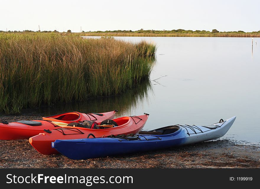 Three colorful kayaks on the shore with beach grass nearby. Three colorful kayaks on the shore with beach grass nearby.