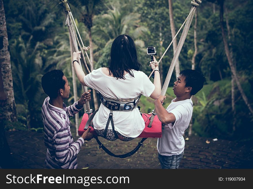 Two Men Assisting Woman Riding on Swing