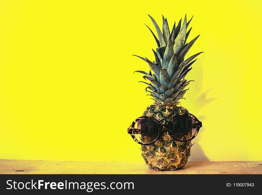 Green Pineapple Fruit With Brown Framed Sunglasses Beside Yellow Surface