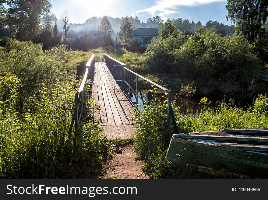 A bridge across a small river in the village in the sun rays