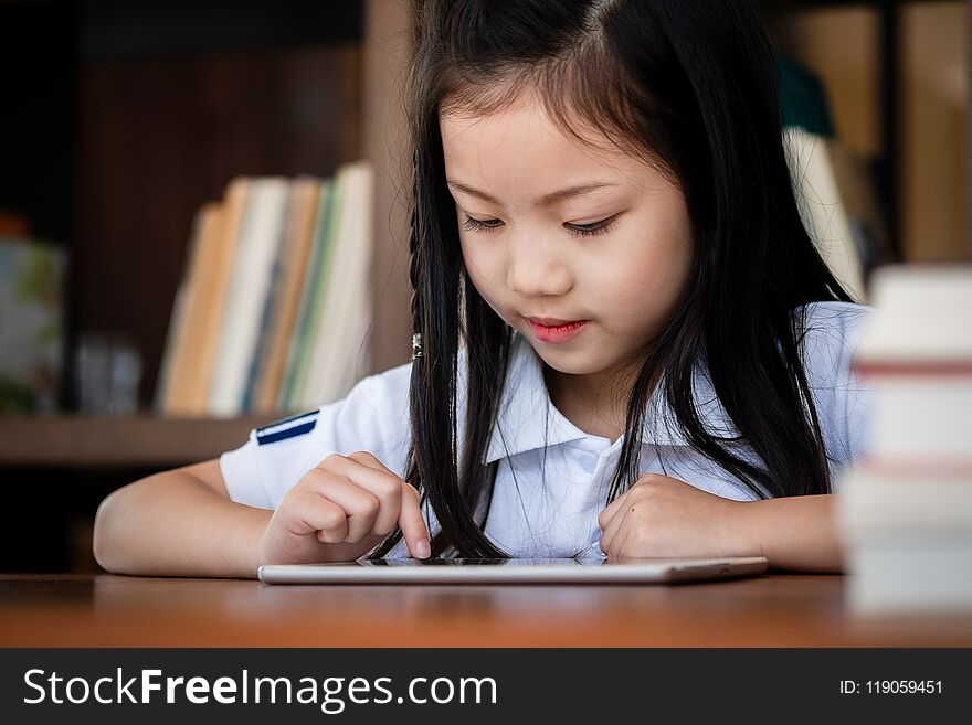 Cute girl smile sitdown and playing laptop computer in the library, children concept, education concept