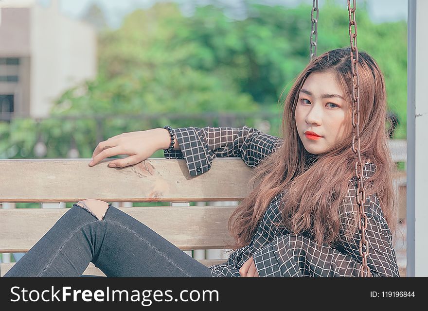 Woman in Black Button-up Long-sleeved Shirt Sitting on Brown Swing Bench