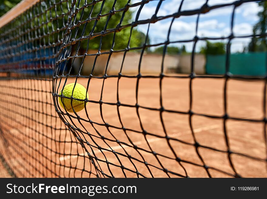 Tennis ball hitting into the net on the court outdoors. Sun is shining. Closeup. Horizontal. Tennis ball hitting into the net on the court outdoors. Sun is shining. Closeup. Horizontal.