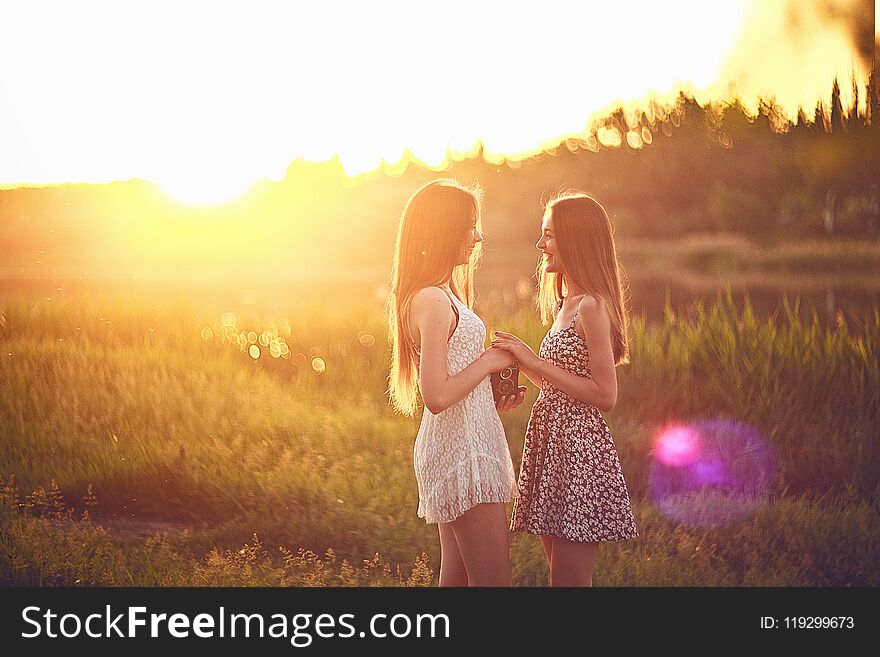 Young female friends standing on grass in sun rays and talking. Concept of friendship and summer vacations. Young female friends standing on grass in sun rays and talking. Concept of friendship and summer vacations.