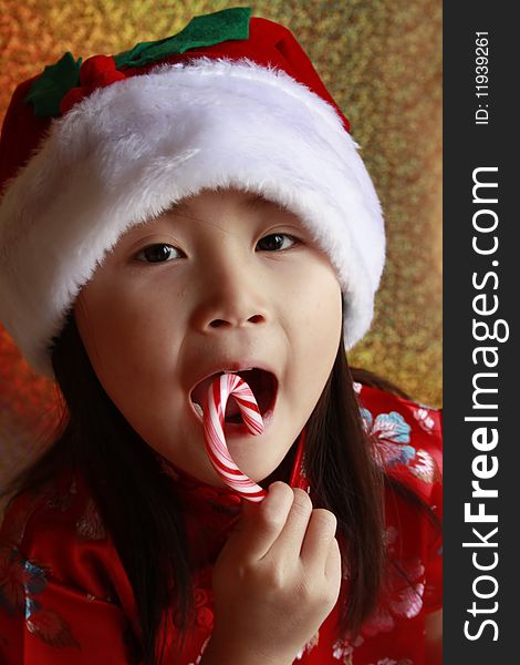 Little asian girl with candy cane with a santa claus hat on.