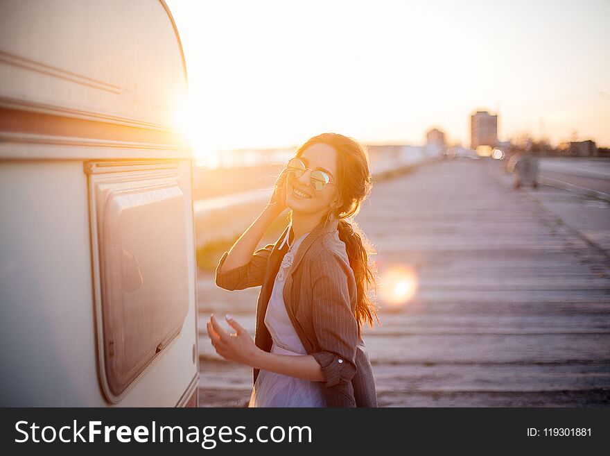 Beautiful young girl in sunglasses on the beach on a summer evening at sunset near trailer.n. Beautiful young girl in sunglasses on the beach on a summer evening at sunset near trailer.n