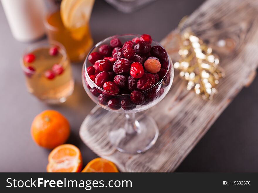 Cranberry in glass bowl on a wooden tray, tangerines, a glass with cider, selective focus.