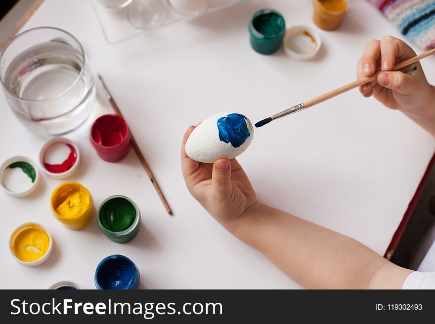 Children`s hands paint Easter eggs. The child is drawing, step by step.