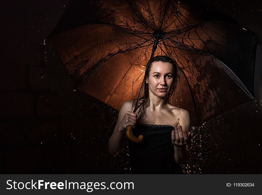 Girl in black dress with umbrella and drops of water during a photoshoot