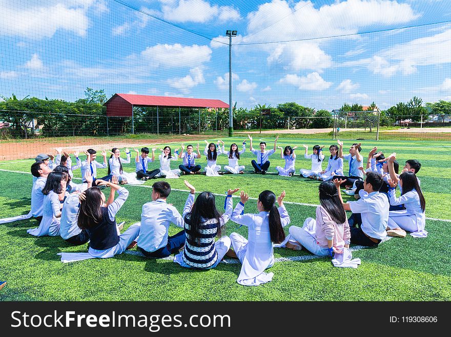 People Sitting on Green Lawn Grass While Doing Hands Up at Daytime