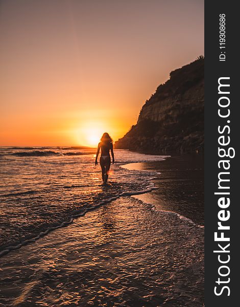 Woman in Bikini on Body of Water Behind Mountain during Golden Hour