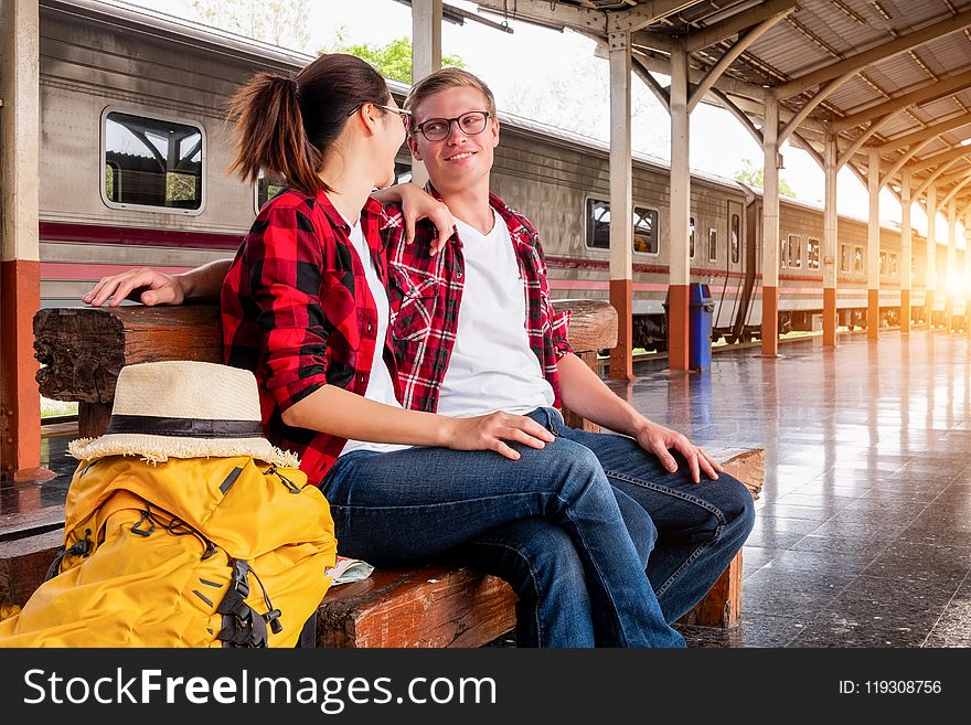 Man and Woman Sitting on Brown Wooden Bench at the Train Station
