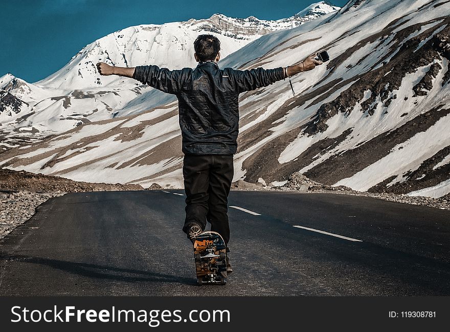 Photo of a Man I the Middle of Road Using Skateboard
