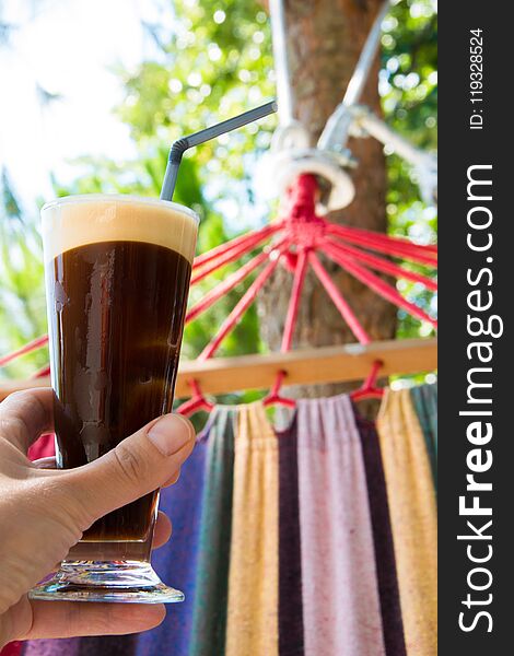 Close up of woman hand female lying on hammock holding glass of cold coffee